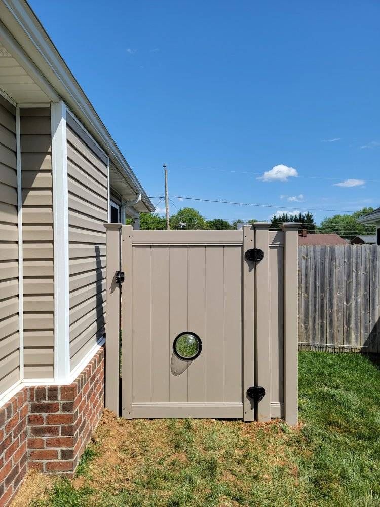 Beige privacy gate in a yard, with a small circular window. Brown siding and brick visible.
