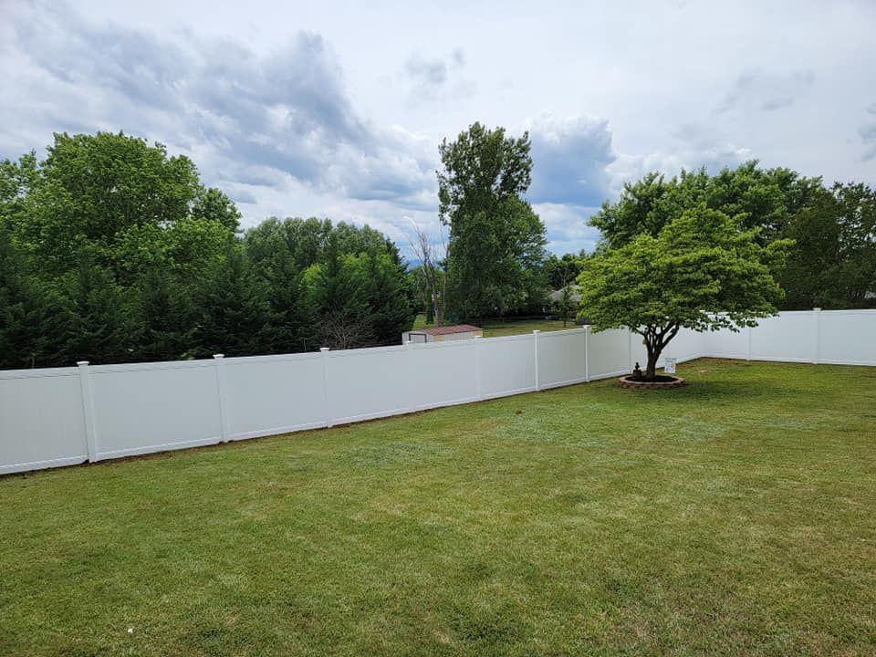 White fence enclosing a green lawn, with trees and a cloudy sky in the background.