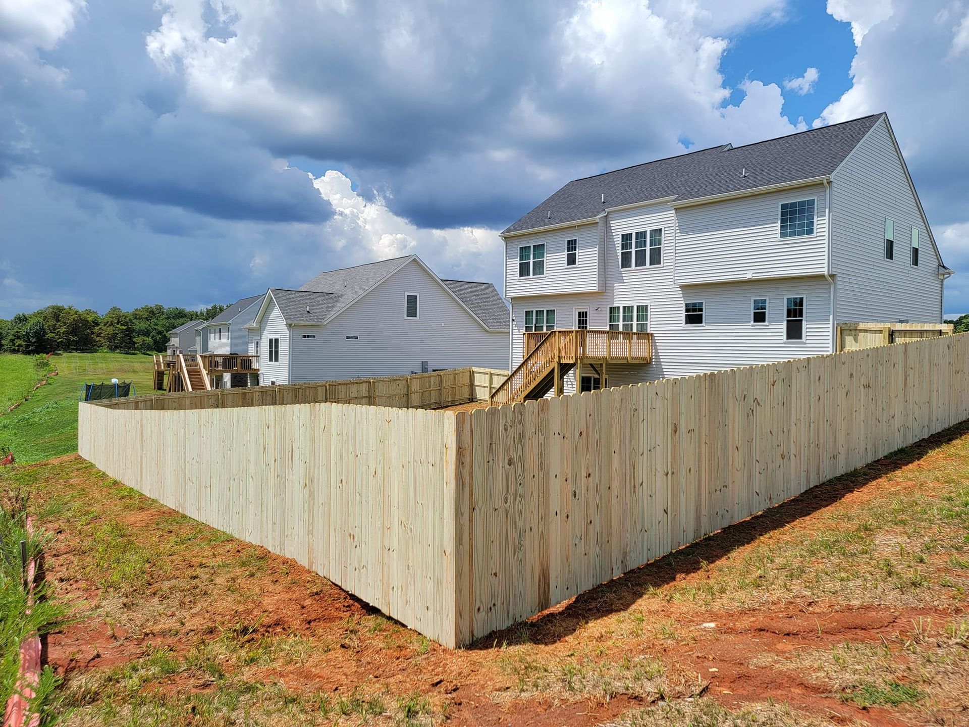Wooden fence surrounds unfinished two-story houses under construction on a sunny day.