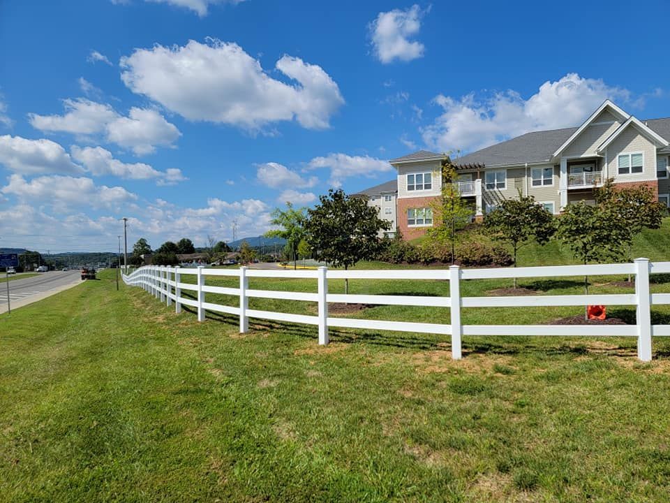 White fence along a grassy area, with apartment buildings and a blue sky with clouds in the background.