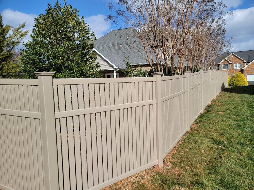 Tan vinyl fence surrounding a grassy yard, with houses in the background.