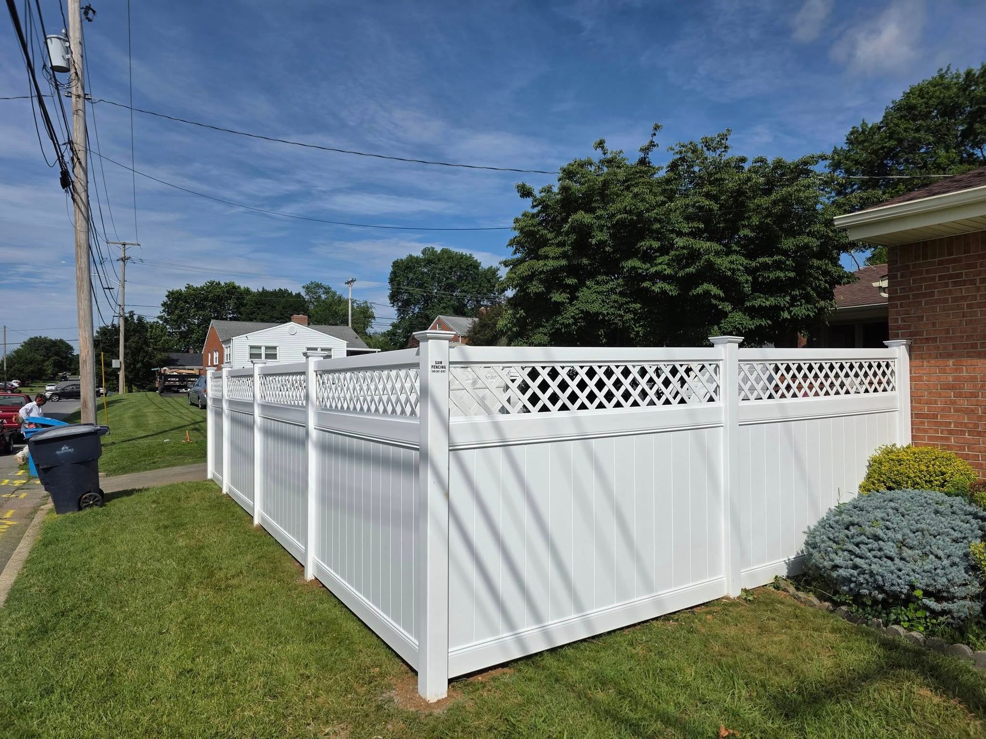 White vinyl fence bordering a green lawn, under a blue sky with a few clouds.