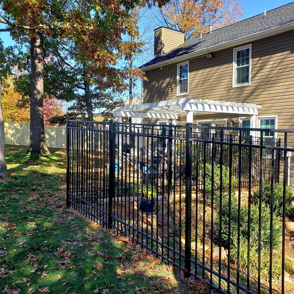 Black metal fence encloses a backyard with a house, pergola, and colorful autumn trees.