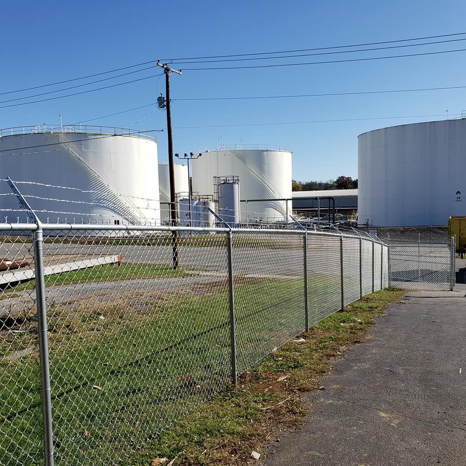 White industrial storage tanks behind a chain link fence, under a blue sky.