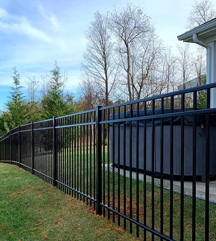 Black metal fence enclosing a backyard with a hot tub, set against a cloudy blue sky.