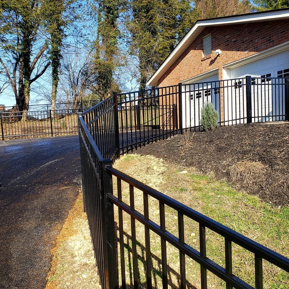 Black metal fence borders a driveway and house with a brick exterior.