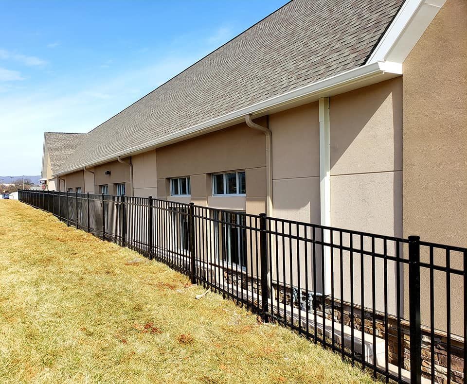 Black metal fence along a building with small windows and a tan exterior. Sunny, blue sky.
