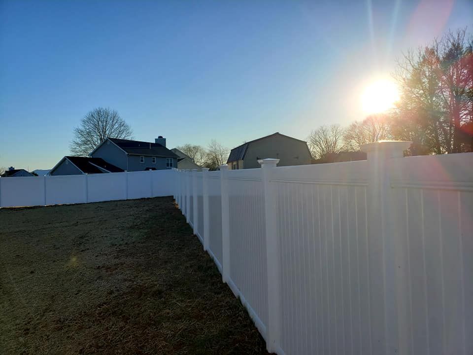 White vinyl fence bordering a yard on a sunny day with houses in the background.