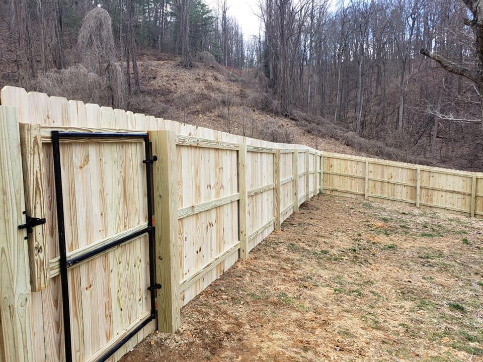 Wooden fence with a gate in a grassy yard, hillside in the background.