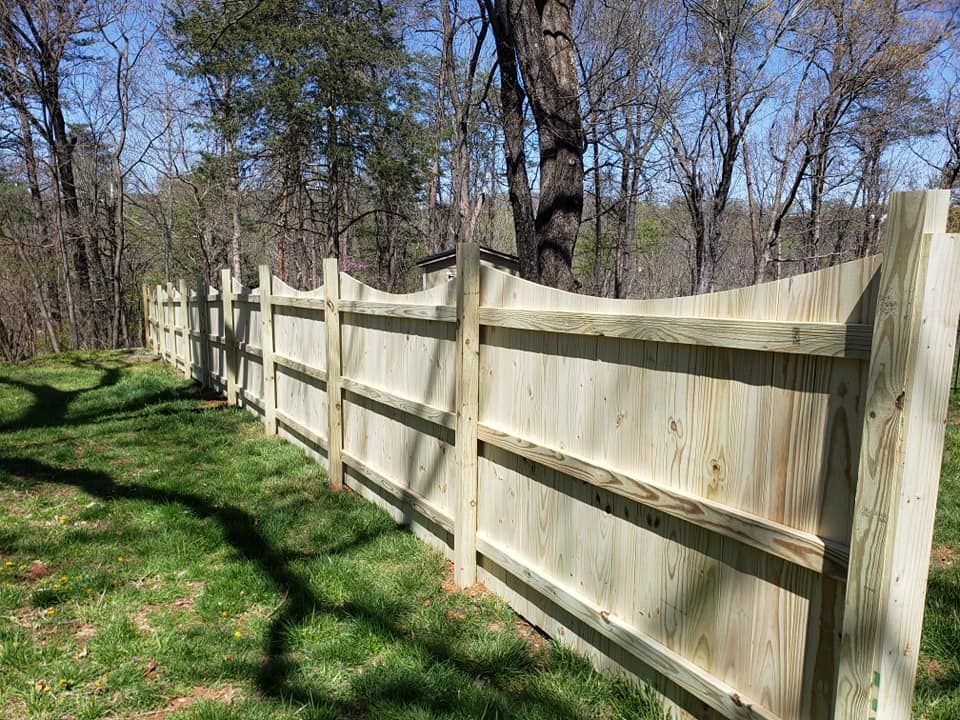Wooden fence in a grassy yard, surrounded by trees.