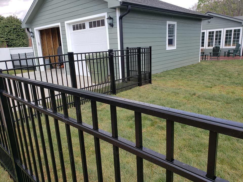 Black metal fence around a yard with green grass and a garage.