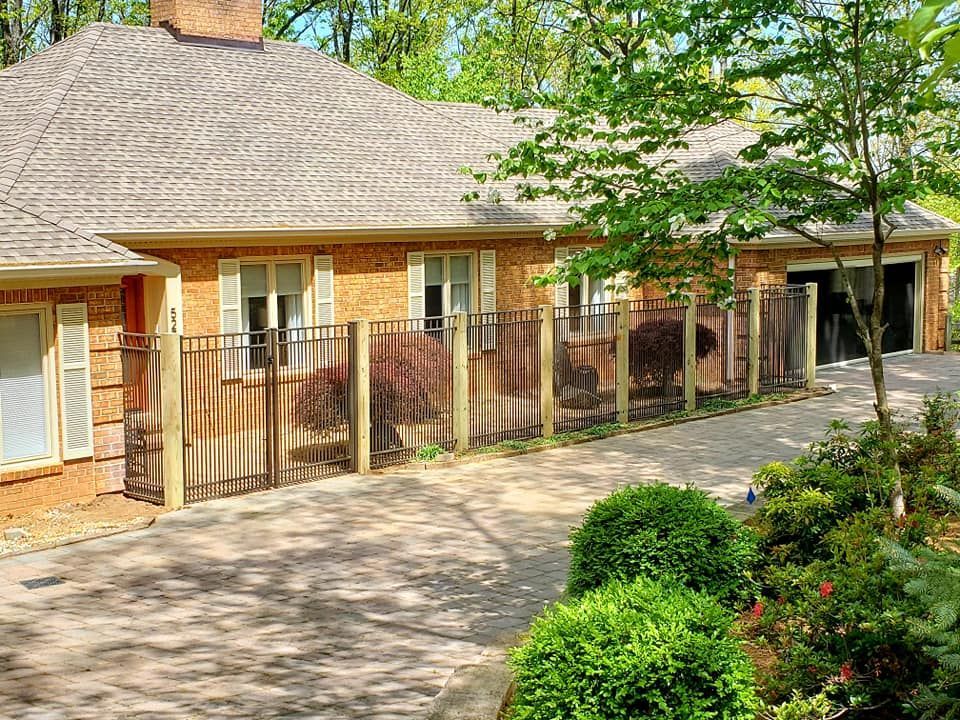 A brick house with a driveway, metal fence, and landscaping.