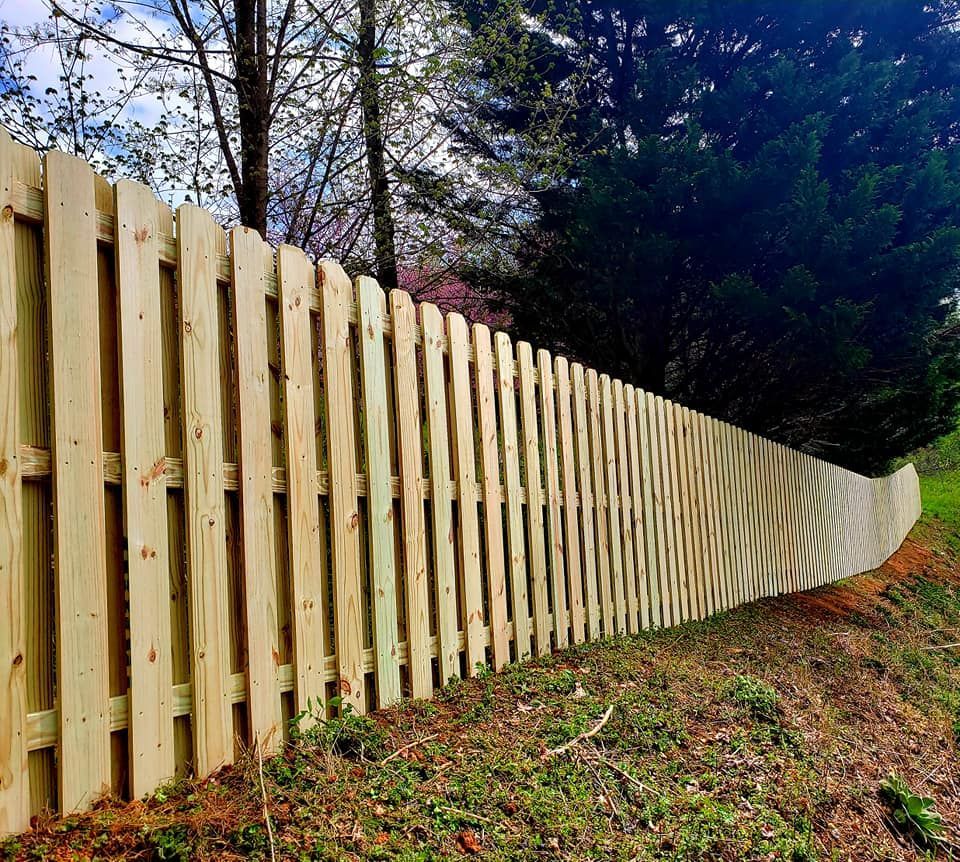 Wooden picket fence on a grassy hillside, trees in the background, angled view.