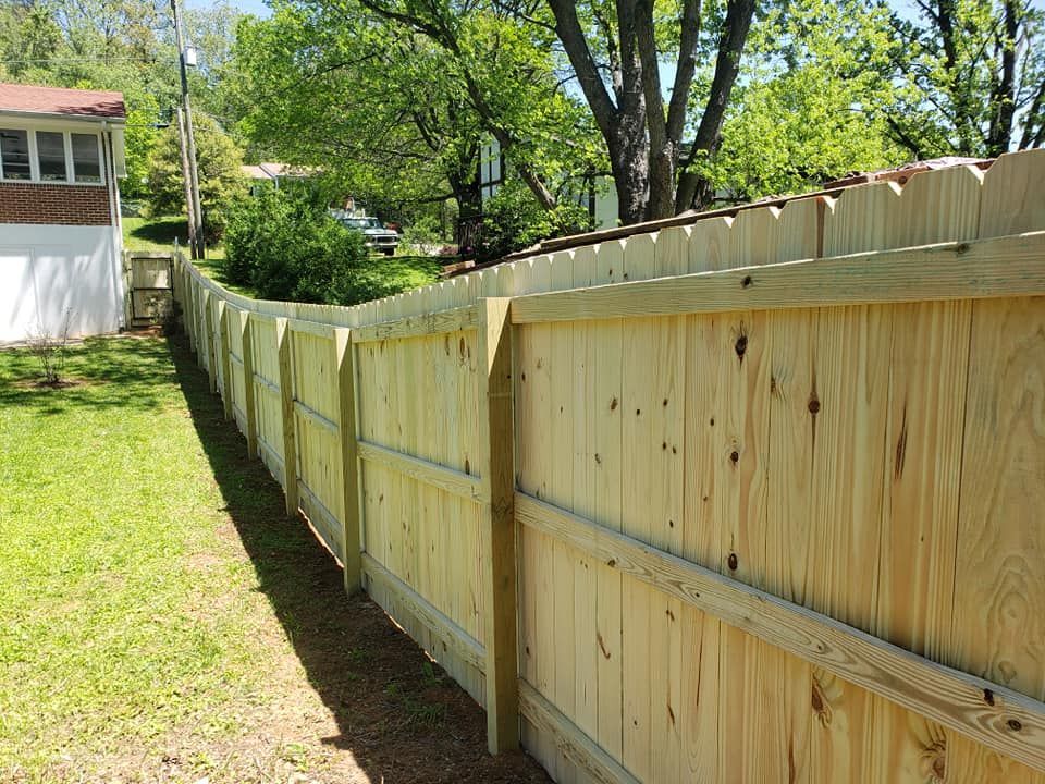 Wooden fence, newly built, runs along a grassy yard, beside a house, on a sunny day.