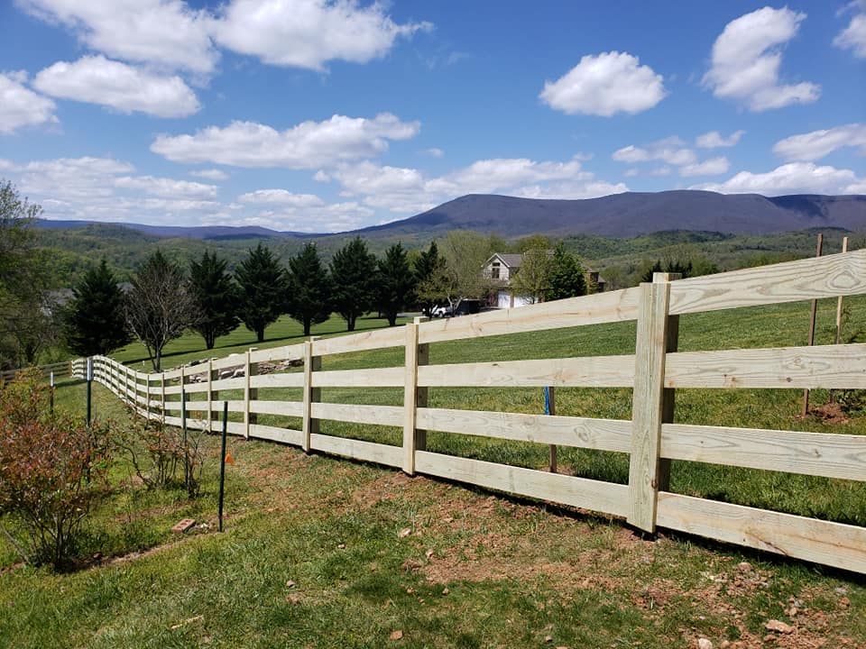 Wooden fence in a grassy field with mountains and blue sky in the background.