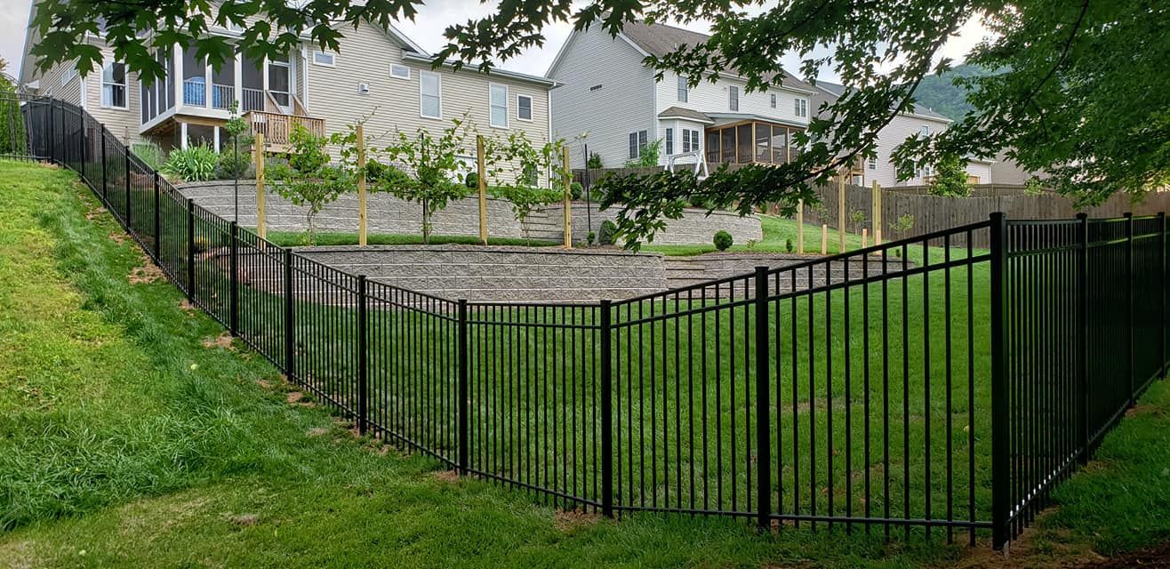 Black metal fence encloses a grassy area near suburban houses on a hillside.
