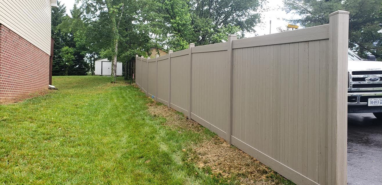 Tan fence along a green lawn beside a building, with a truck parked on the right.