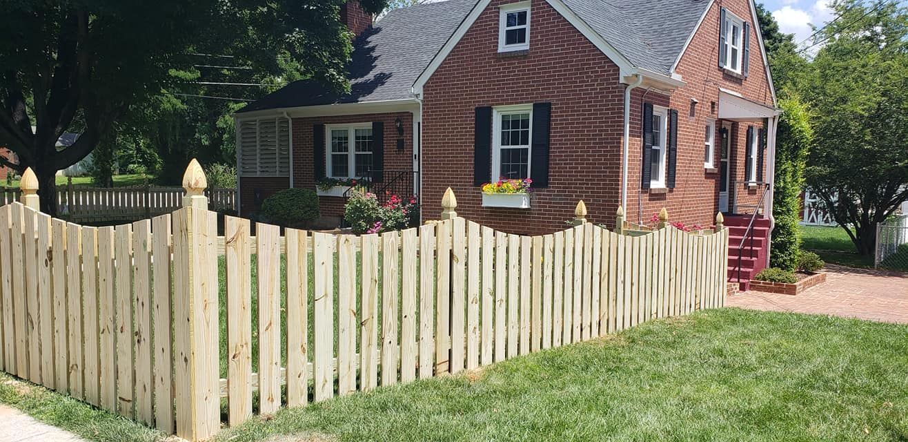 A two-story brick house behind a wooden picket fence on a grassy lawn.