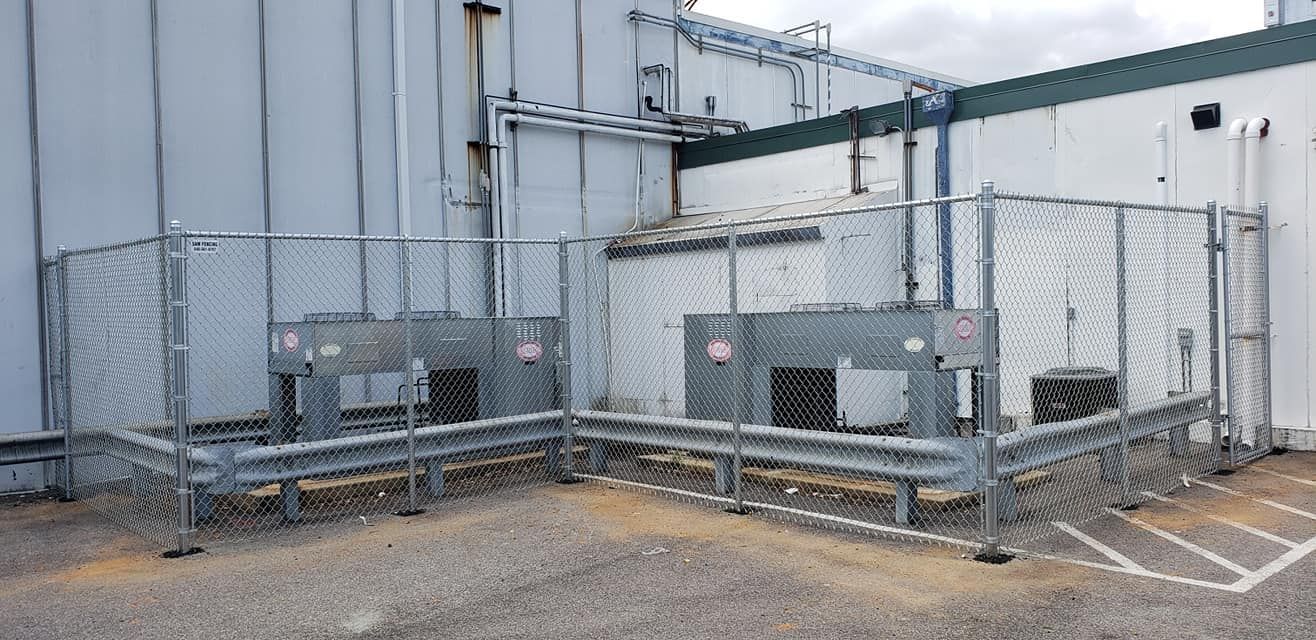 Two gray electrical boxes behind chain link fence. Building in the background. Parking lines visible.