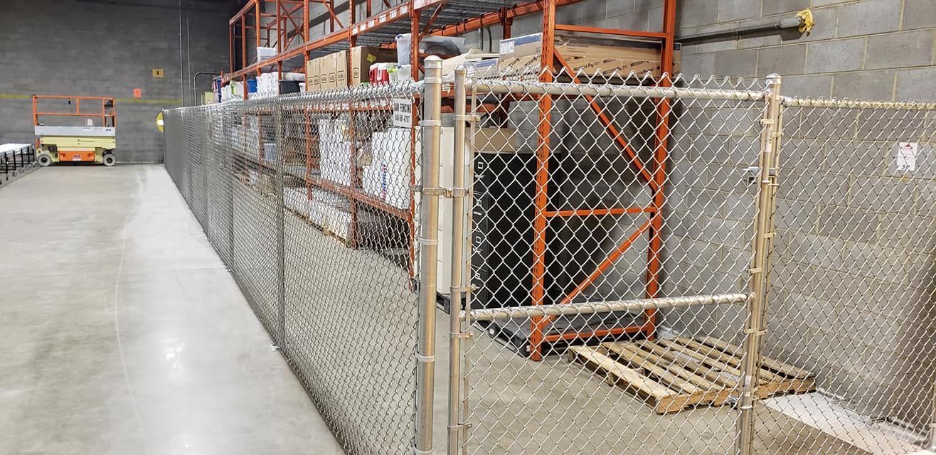 Warehouse interior with a chain-link fence separating a concrete floor from shelves and a forklift.