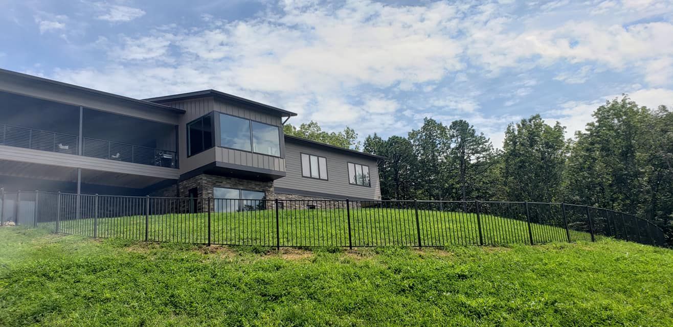 House with a vineyard on a grassy hill; trees in the background, cloudy sky.