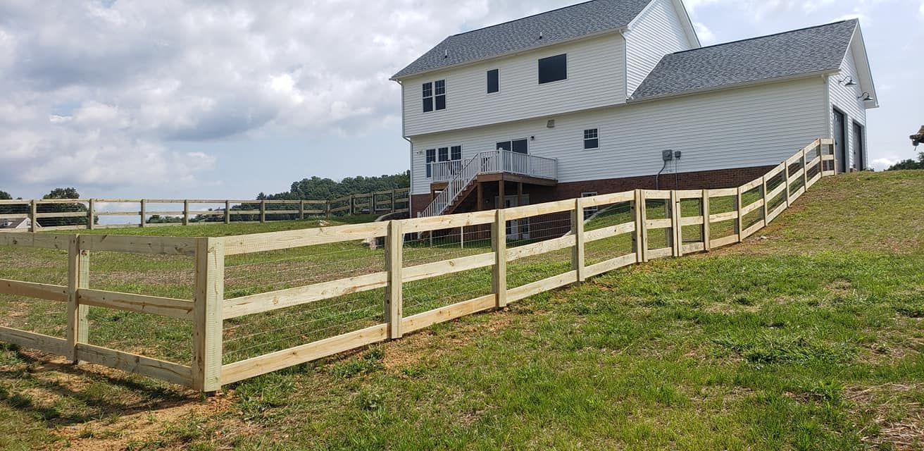 A wooden fence surrounds a grassy yard, with a two-story white house in the background under a cloudy sky.