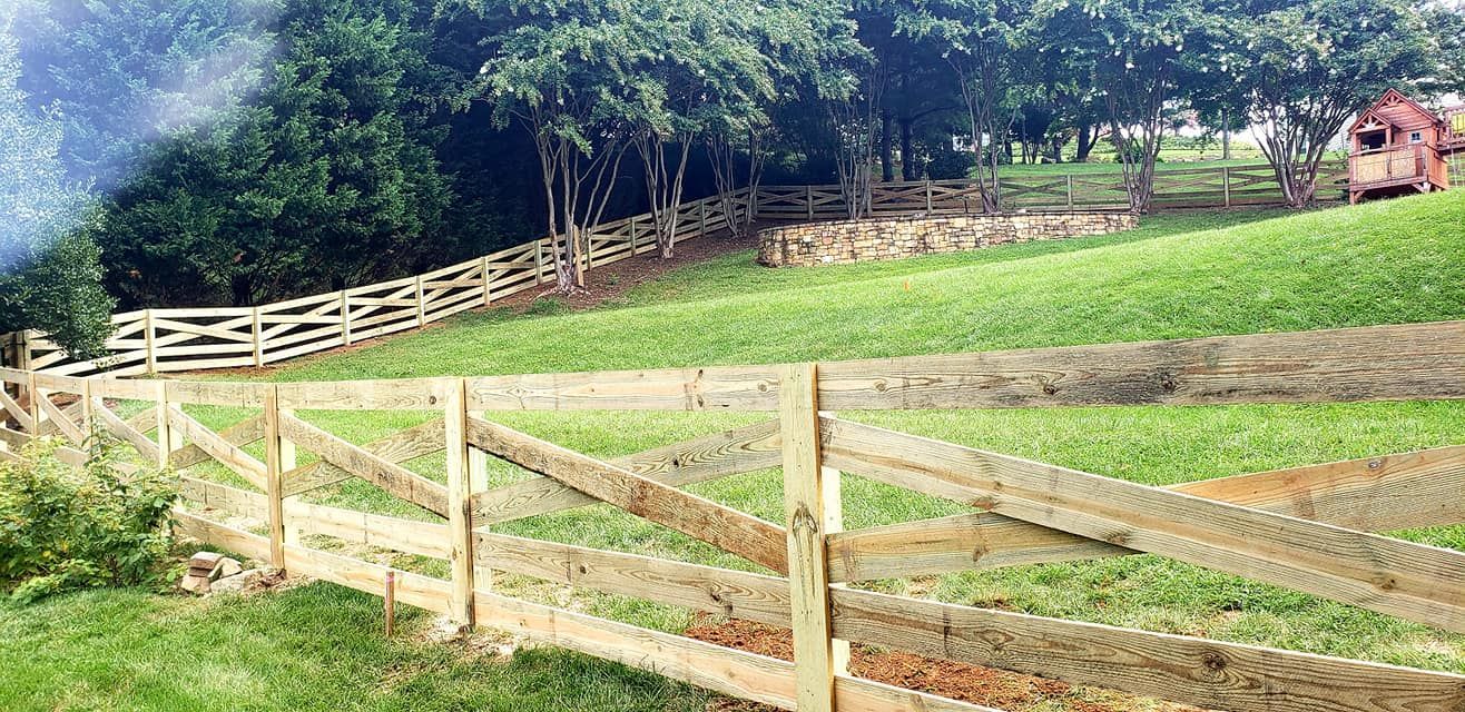 Wooden fences on a grassy hillside, trees in the background, a small red structure.