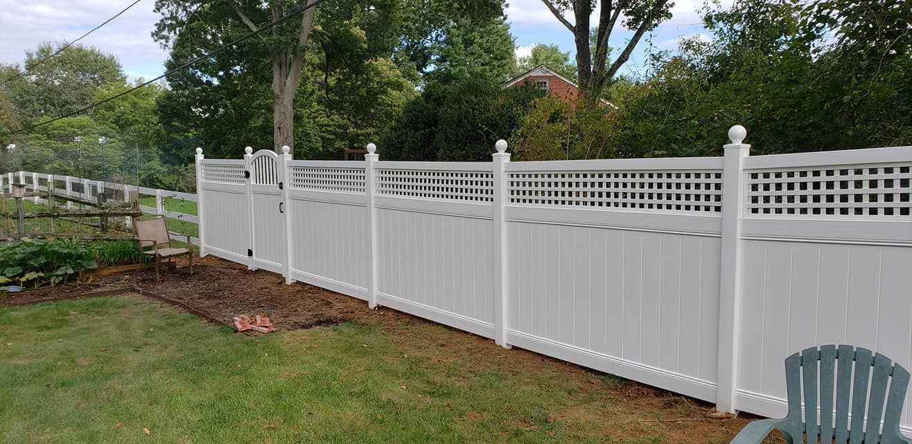 White vinyl fence in a backyard setting with green grass and trees.