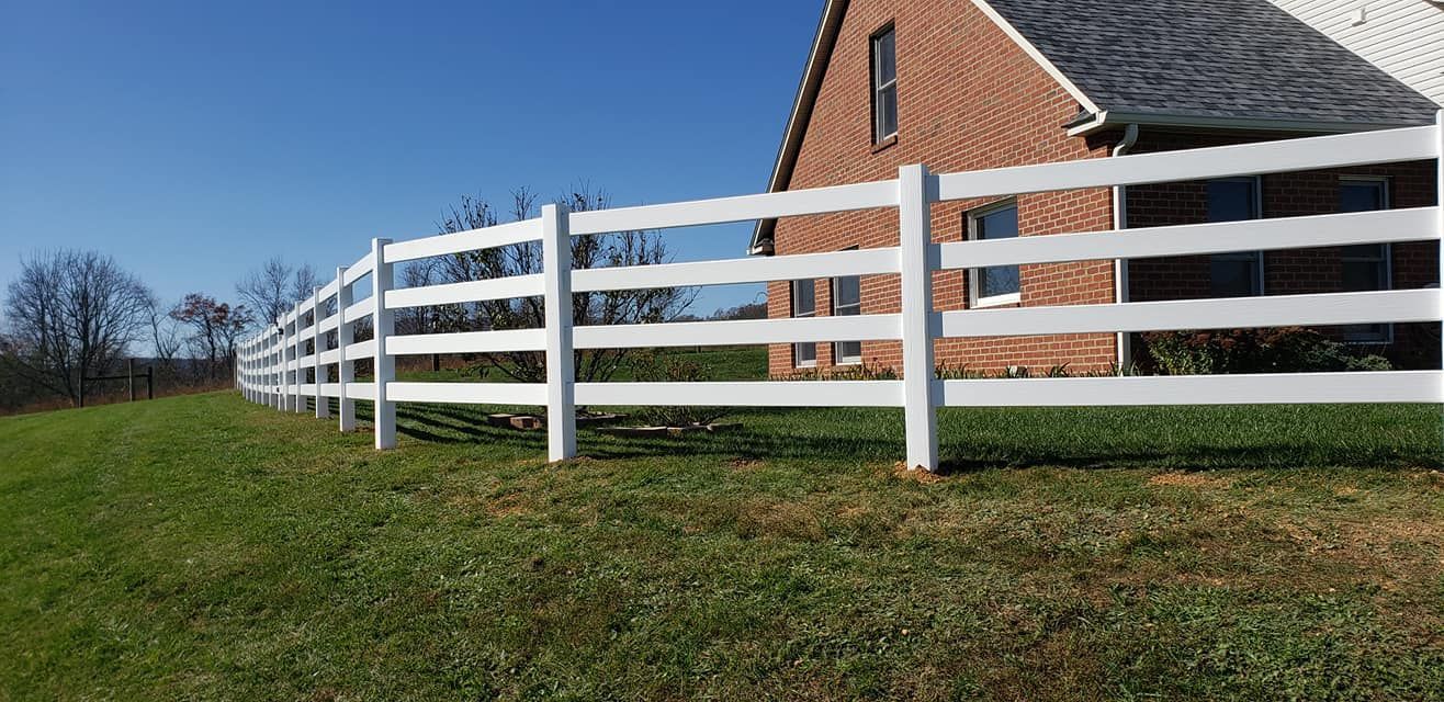 White fence in front of a brick house on a grassy lawn under a clear blue sky.
