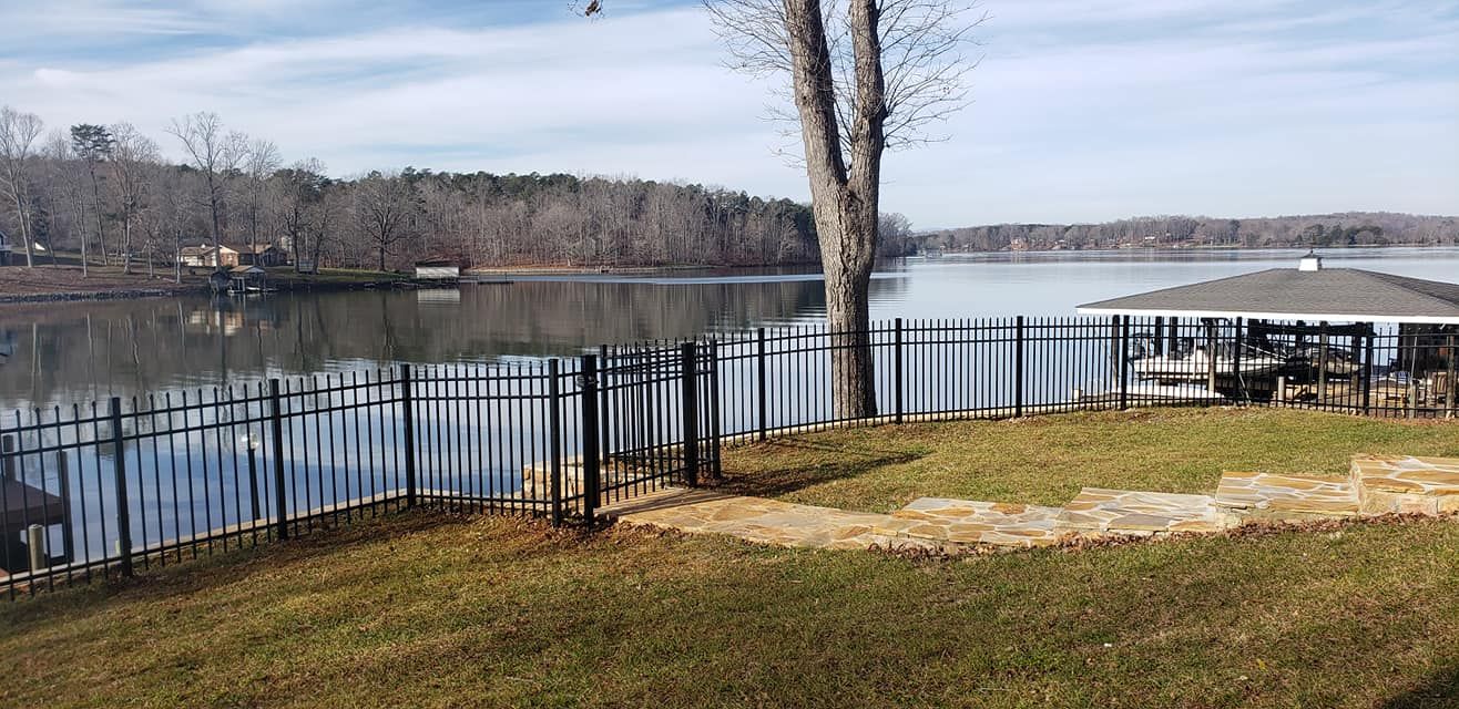 Lakefront scene with trees, fence, and a covered patio on a sunny day.