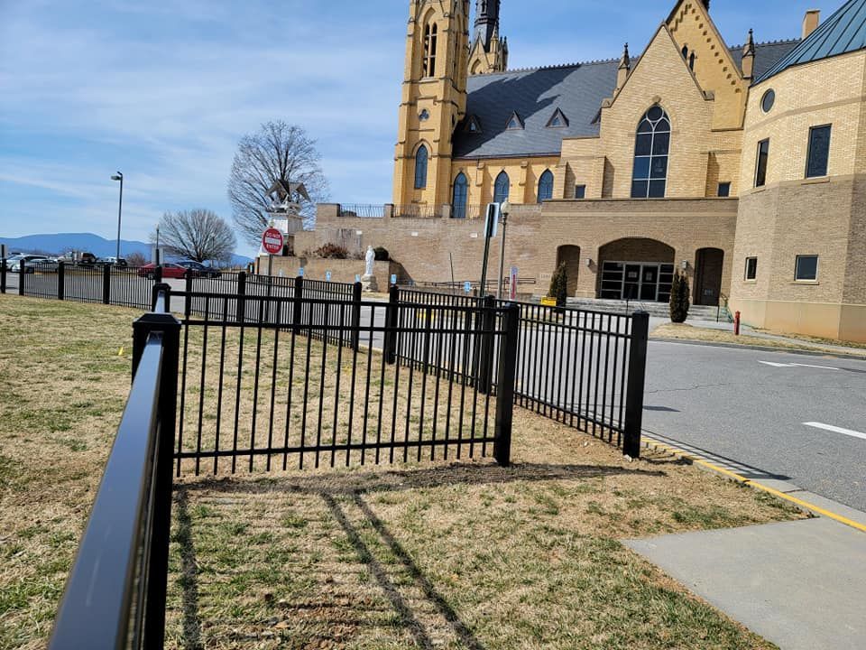 Black metal fence in front of a yellow brick church with a tall steeple. Sunny day.