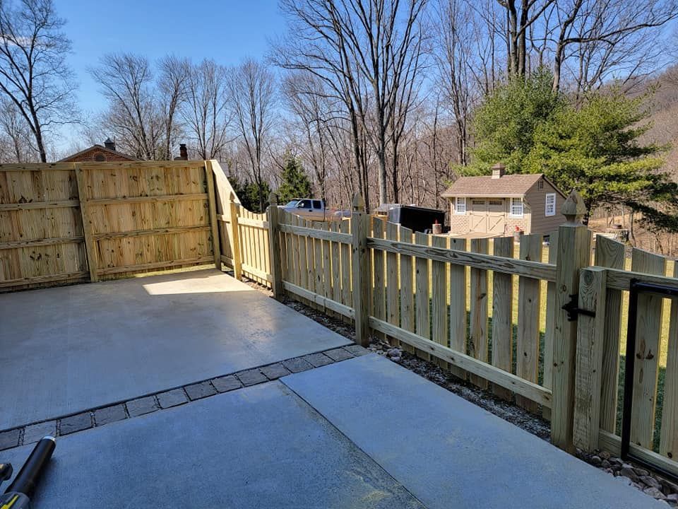 A new wooden fence surrounds a concrete patio on a sunny day.