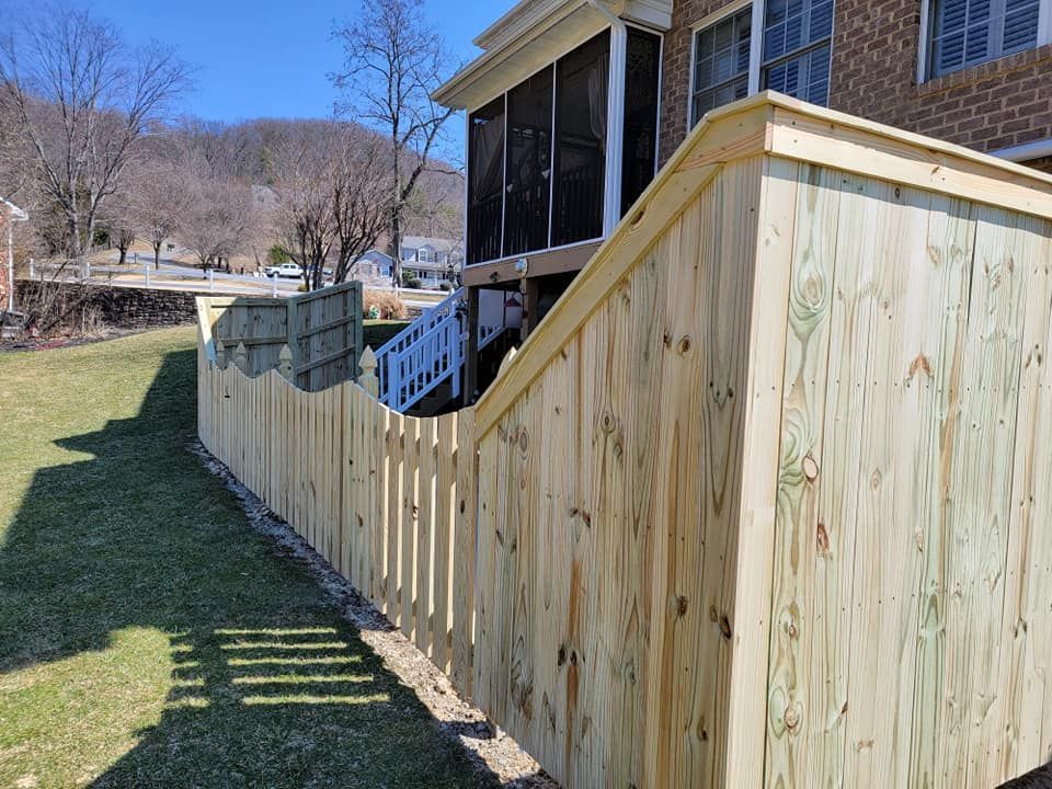 A new wooden fence built along a grassy yard, beside a house with a screened porch and white stairs.