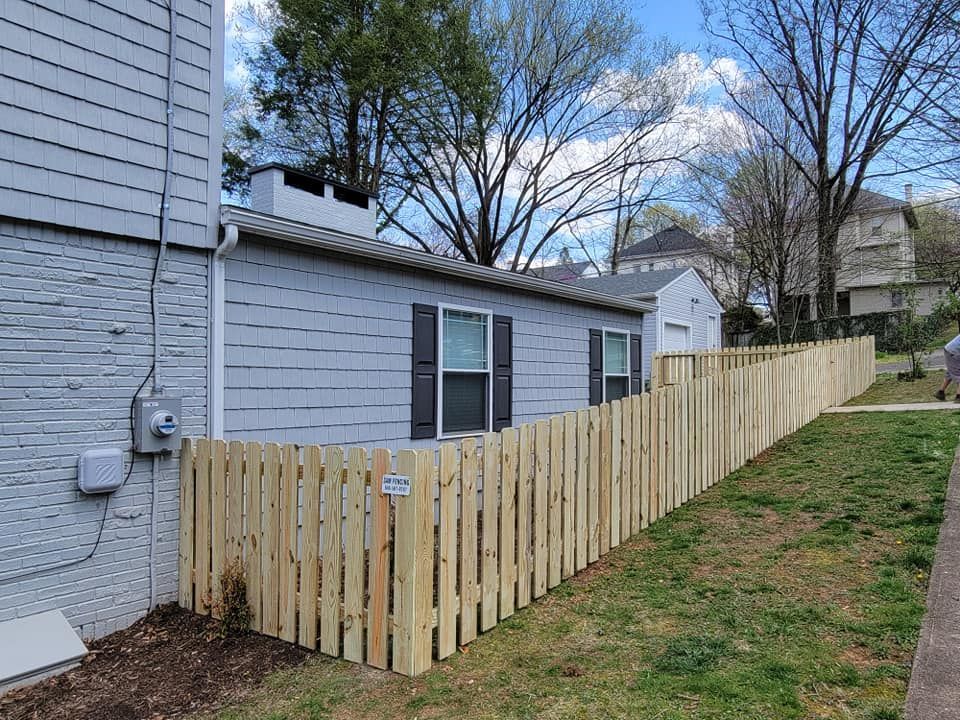 New wooden picket fence along a grassy yard next to a gray building.