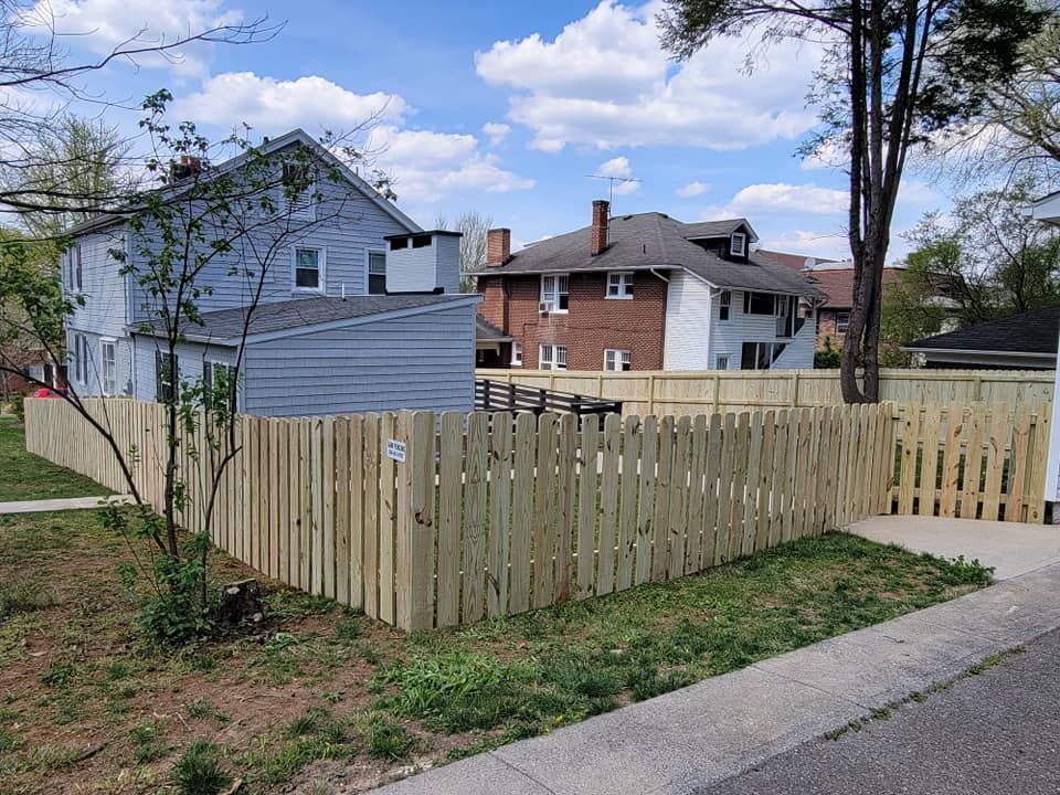 Wooden fence surrounding yard in front of two-story houses; sunny day.