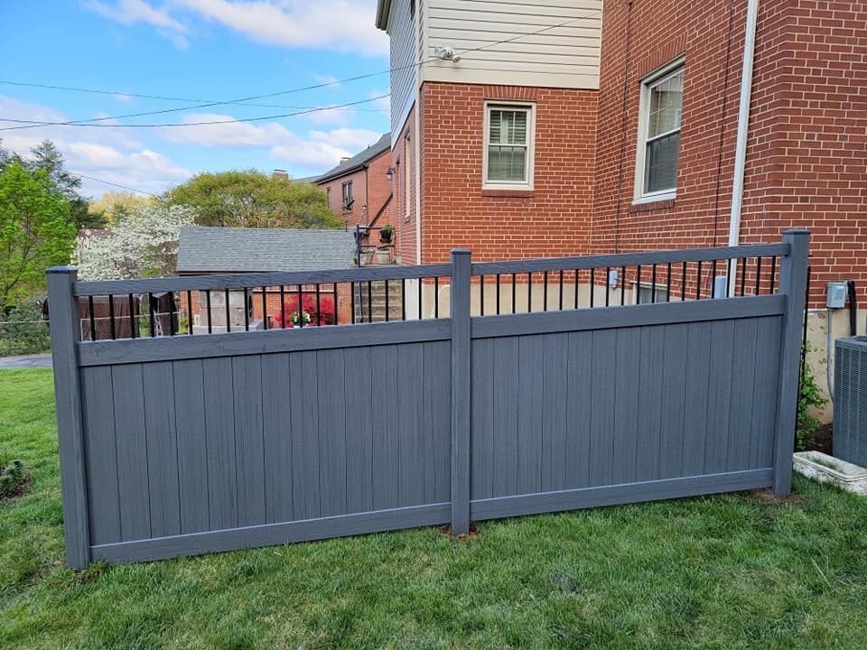 Gray vinyl privacy fence against a brick building, on a green lawn.