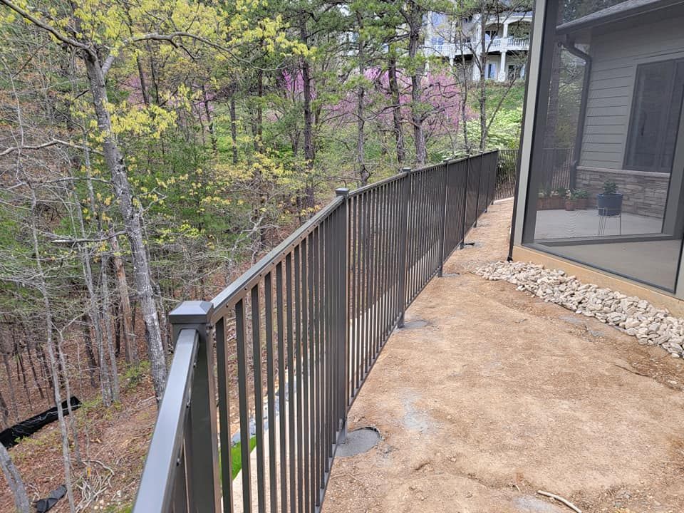 Metal railing on a raised outdoor deck with a wooded background and screening.