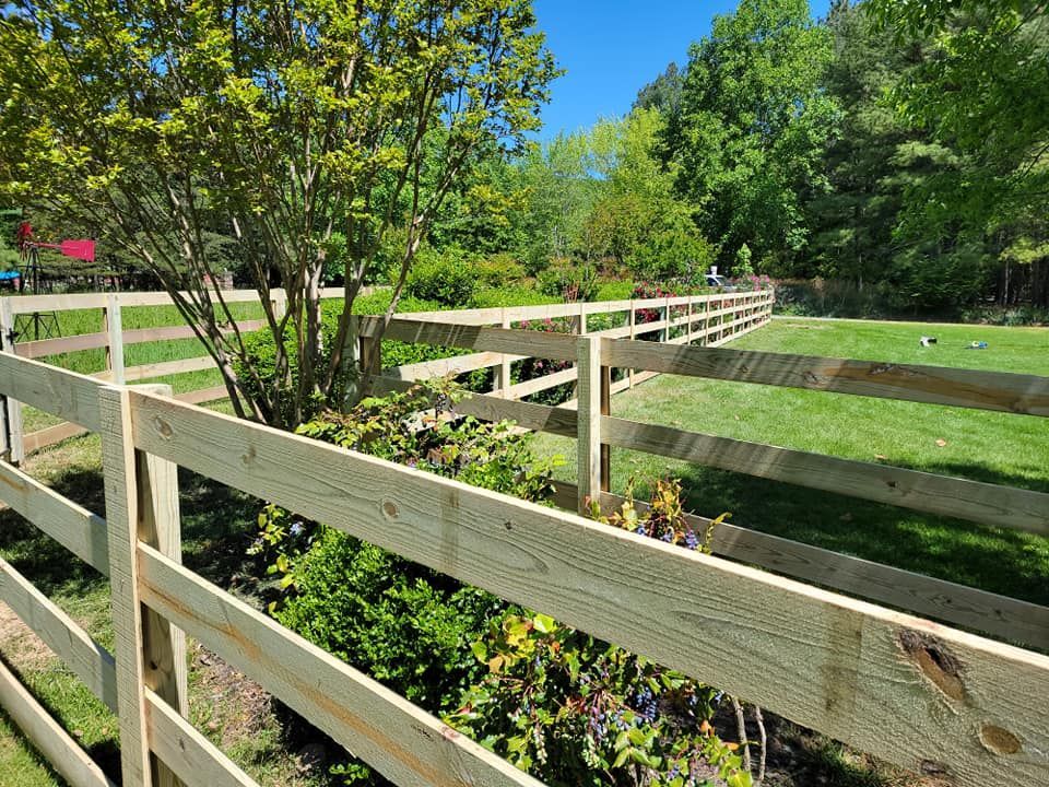 Wooden fence surrounding a grassy yard with trees and blue sky.