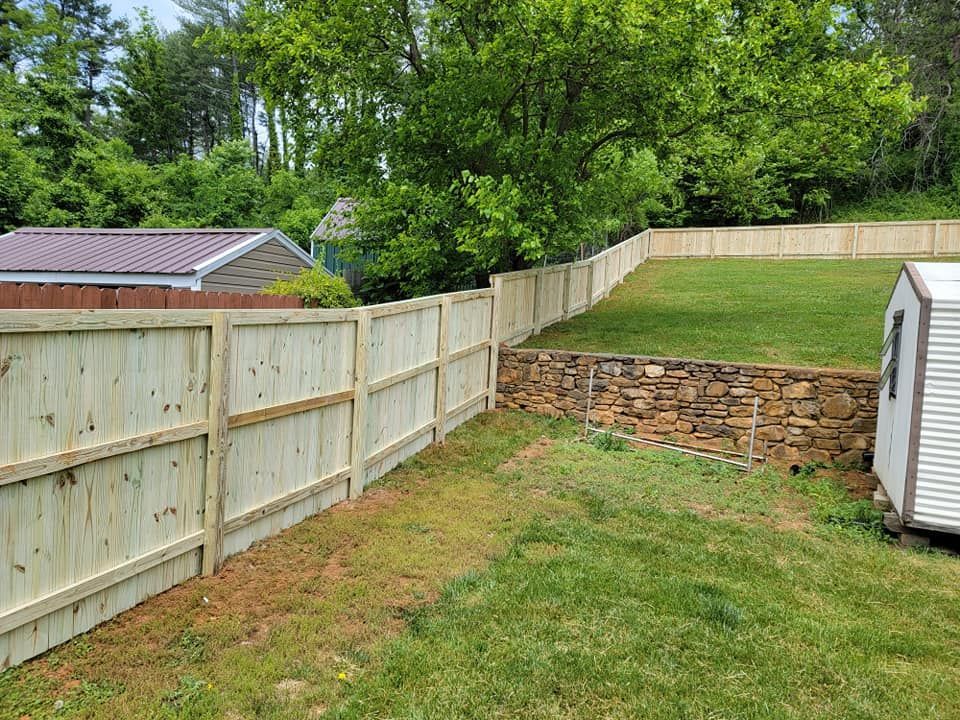 Backyard with a wooden fence, retaining wall, shed, and green grass.