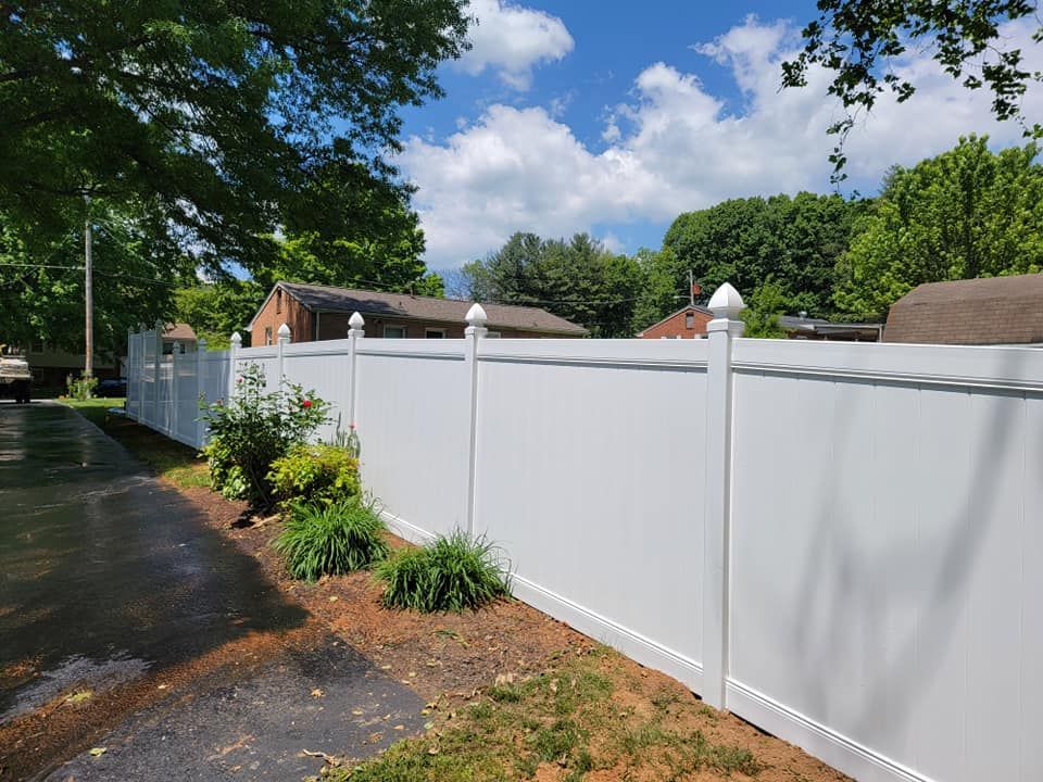 White vinyl fence with decorative post tops along a residential street under a bright, sunny sky.