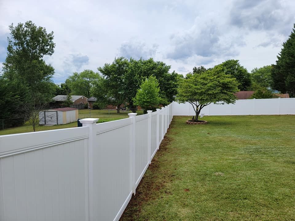 White vinyl fence bordering a grassy backyard with trees and cloudy sky.