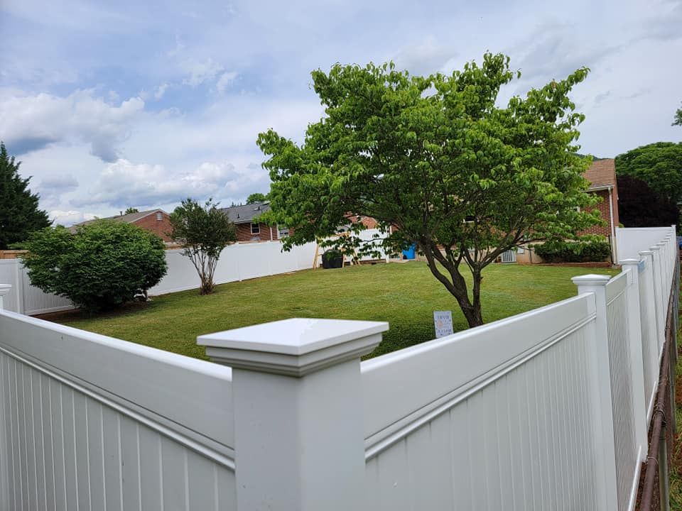 White fence encloses a green lawn with trees and a cloudy sky in a residential backyard setting.