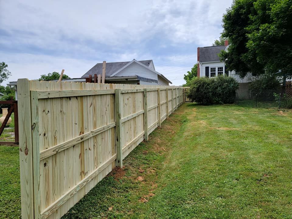 Wooden fence in a grassy yard, with houses in the background under a cloudy sky.