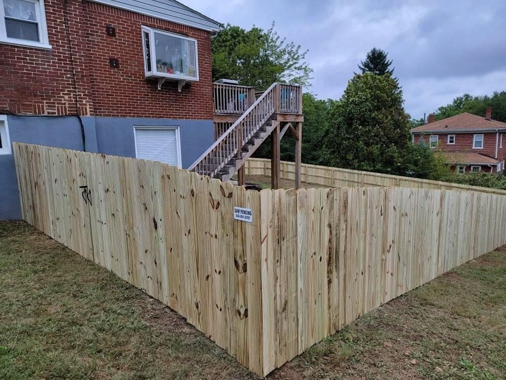 Wooden fence surrounding a backyard with a deck and brick house.