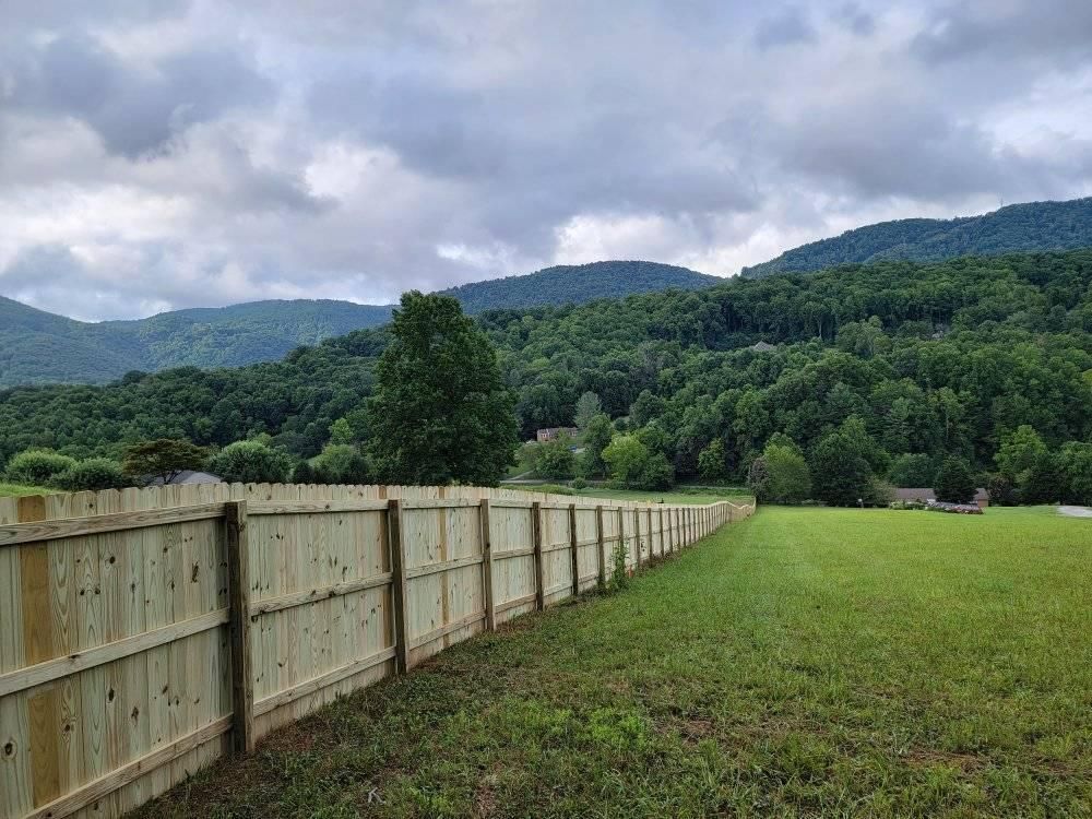 Wooden fence bordering a grassy field, mountains in the background under a cloudy sky.