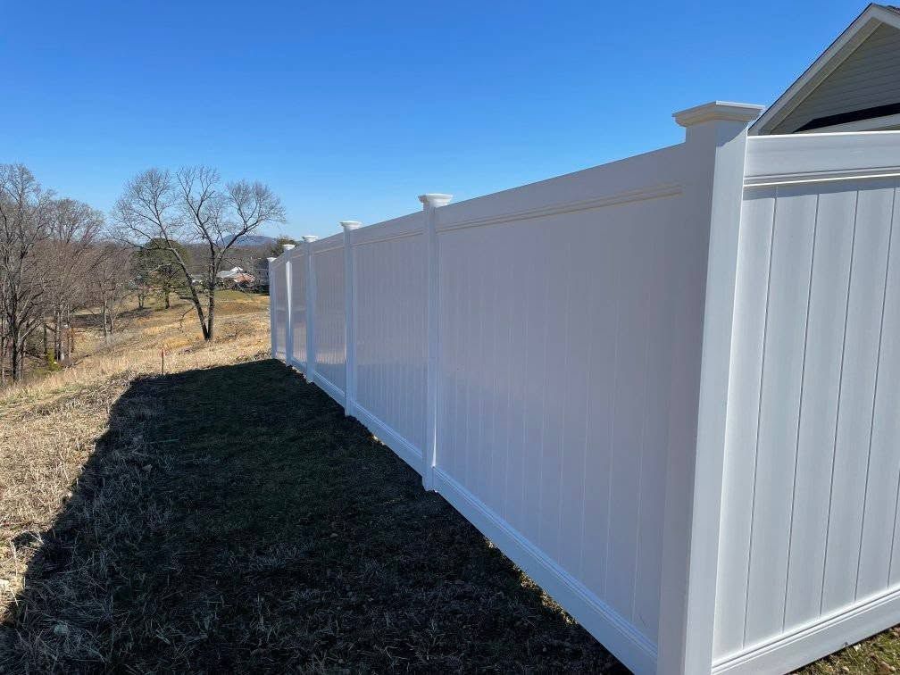 White vinyl fence along grassy terrain under a clear blue sky.