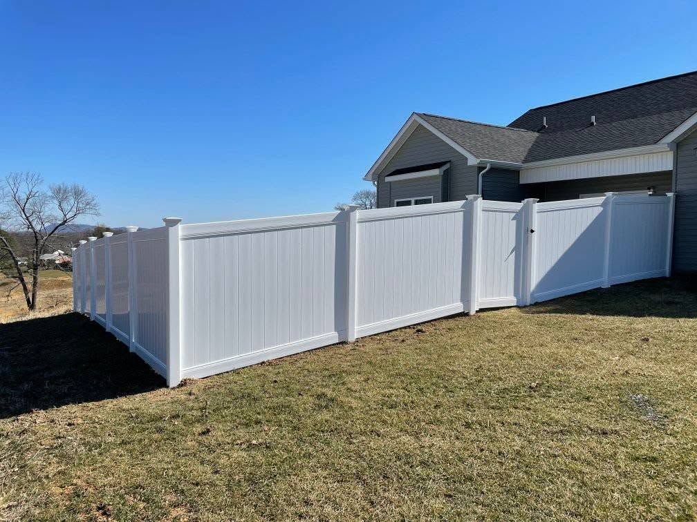 White vinyl fence enclosing a grassy yard, beside a house, under a blue sky.
