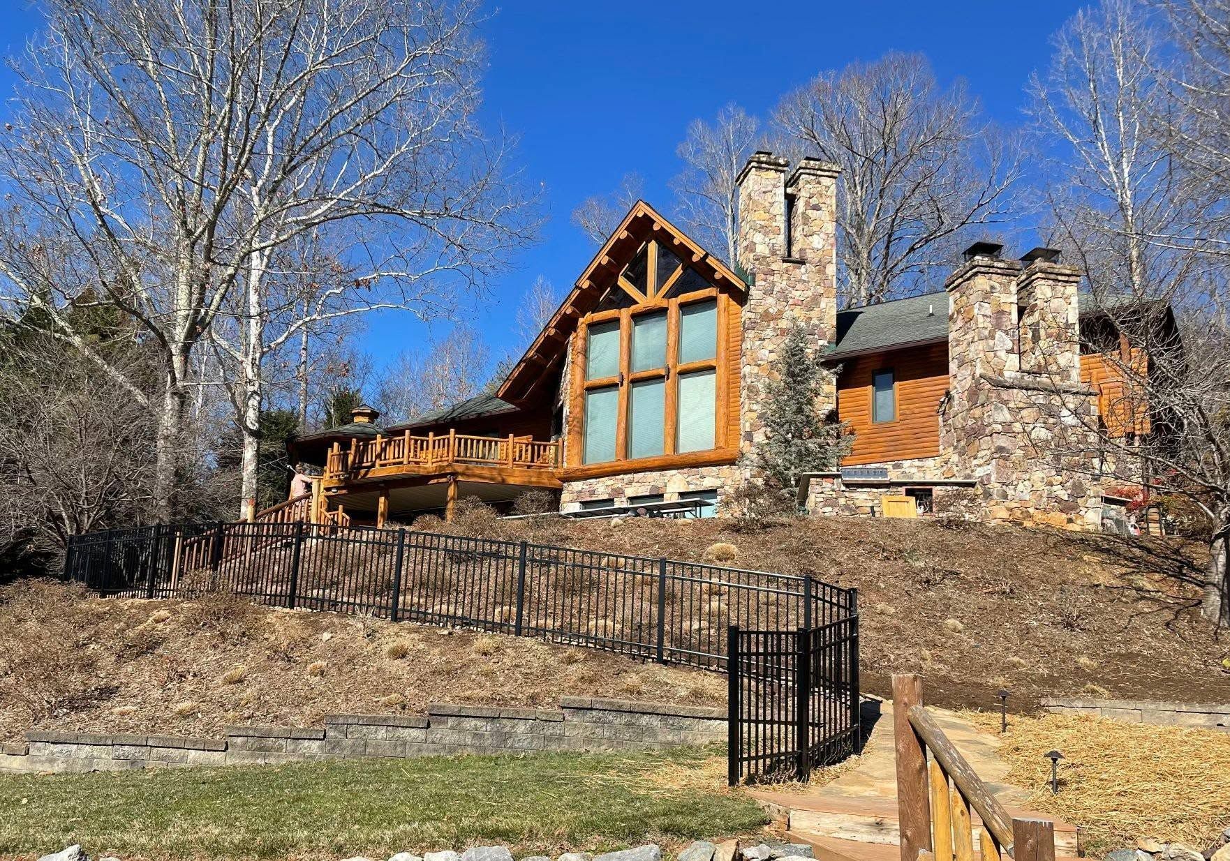 A large cabin-style house with stone chimneys and a wooden facade sits on a hillside.