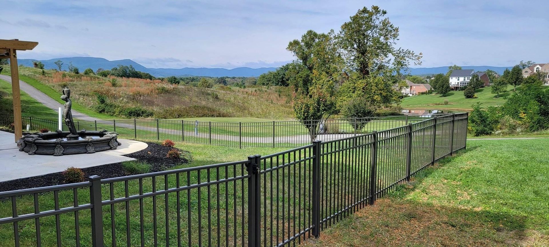 A scenic outdoor view featuring a black metal fence, water feature, and rolling hills under a blue sky.