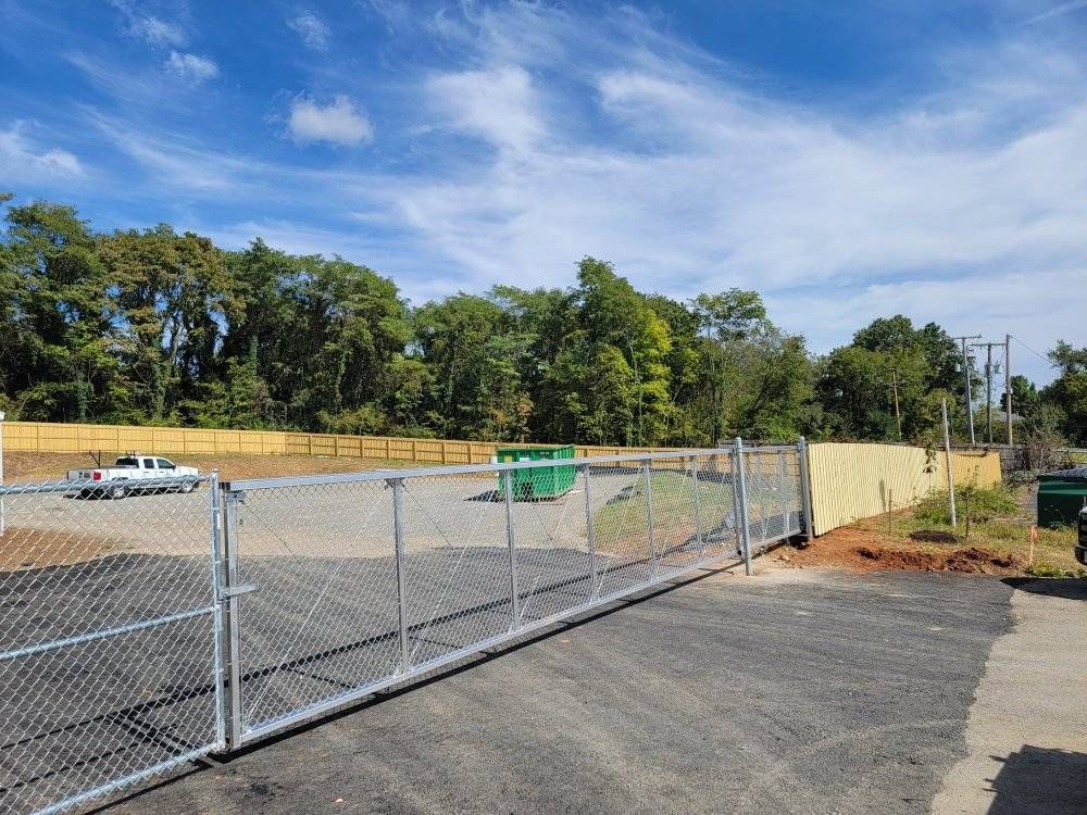 A fenced-in gravel lot with a chain-link gate. Trees and a blue sky are in the background.